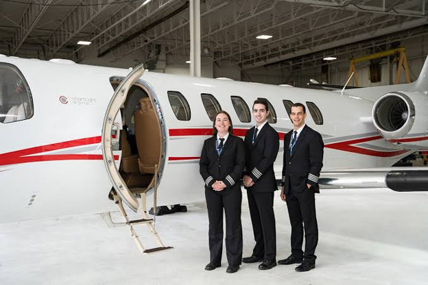 Flight crew in uniform posing in front of a private airplane inside an illuminated hangar